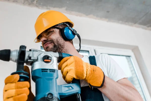 Selective focus of handyman in helmet and yellow gloves using hammer drill — Stock Photo