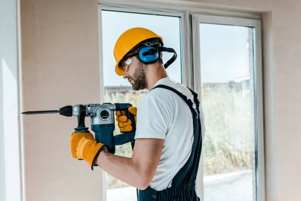 Handyman in helmet and yellow gloves using hammer drill — Stock Photo