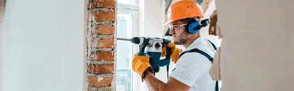 Tiro panorâmico de faz-tudo em luvas uniformes e amarelas usando broca de martelo — Fotografia de Stock