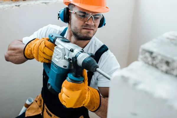 Enfoque selectivo del manitas guapo en guantes uniformes y amarillos con taladro de martillo - foto de stock