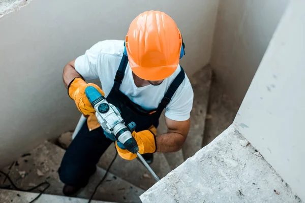 Vista aérea del trabajador en guantes uniformes y amarillos con taladro de martillo - foto de stock