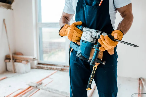 Cropped view of workman in yellow gloves holding hammer drill — Stock Photo