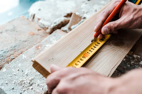 Vista recortada del manitas sosteniendo lápiz mientras mide tablón de madera - foto de stock