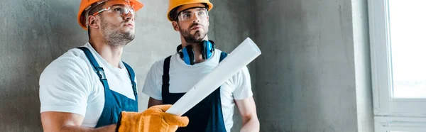 Plano panorámico de reparador guapo sosteniendo rollo de papel cerca de compañero de trabajo - foto de stock