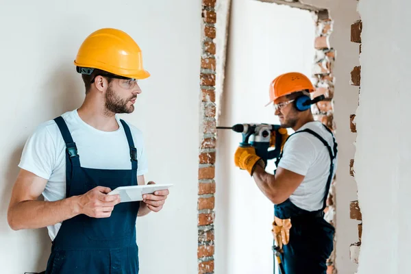 Selective focus of handyman holding digital tablet while coworker working in house — Stock Photo