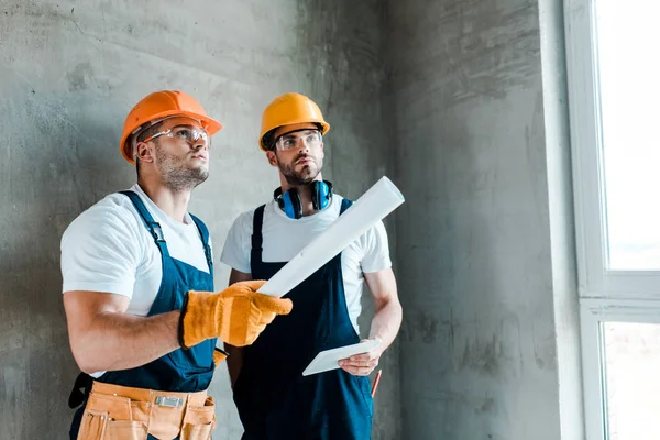 Handsome repairman holding digital tablet near coworker with paper roll — Stock Photo