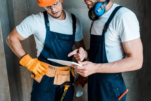 Vista recortada del reparador barbudo apuntando con el dedo a la tableta digital cerca de compañero de trabajo - foto de stock