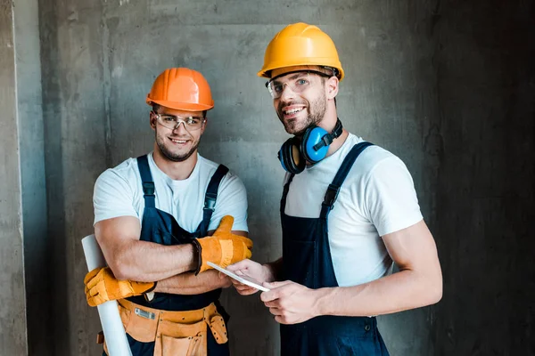 Счастливые ремонтники в очках и шлемах, стоящие в доме — стоковое фото