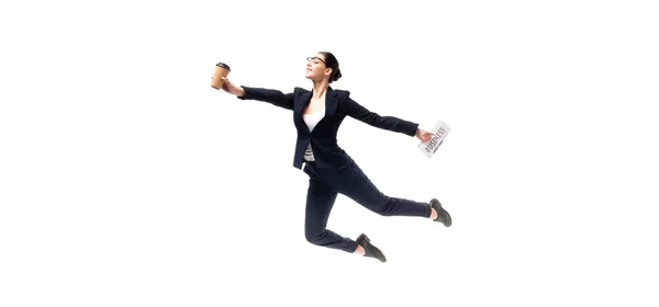 Panoramic shot of beautiful businesswoman holding newspaper and paper cup while levitating isolated on white — Stock Photo