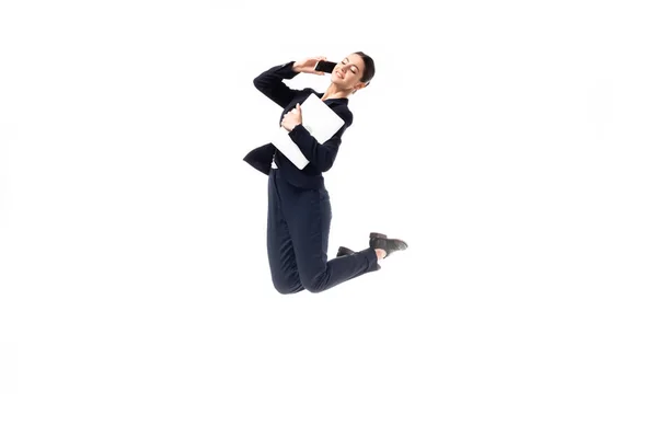 Sonriente mujer de negocios bailando mientras habla en el teléfono inteligente y la celebración de portátil aislado en blanco - foto de stock