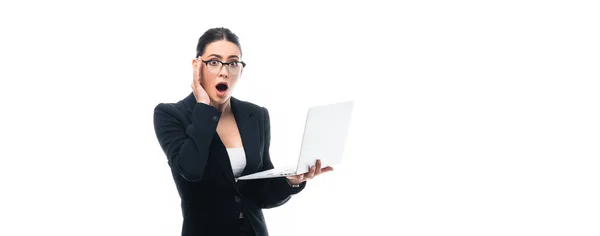 Панорамний знімок шокованої бізнес-леді тримає ноутбук, дивлячись на камеру ізольовано на білому — стокове фото