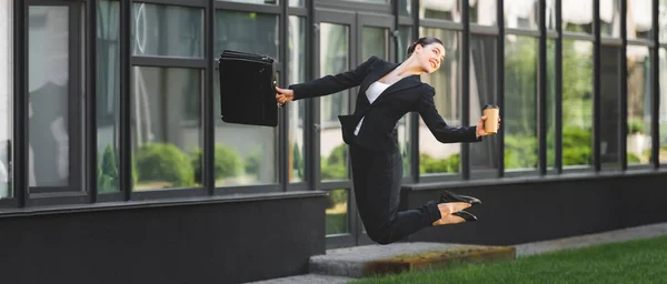 Panoramaaufnahme einer glücklichen Geschäftsfrau, die schwebt, während sie Pappbecher und Aktentasche hält — Stockfoto