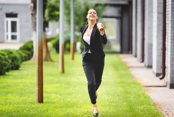 Heureuse jeune femme d'affaires courir près de l'immeuble de bureaux tout en tenant du café pour aller — Photo de stock