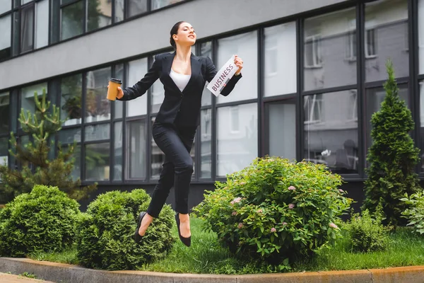 Graceful businesswoman levitating while holding newspaper and paper cup — Stock Photo