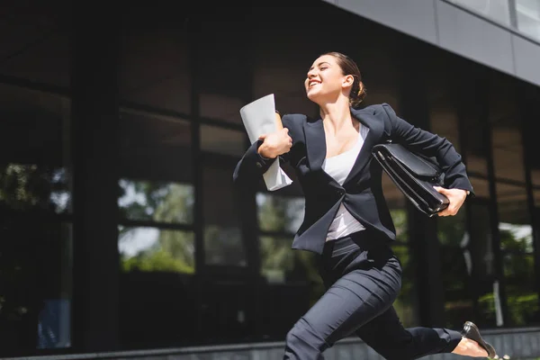 Happy businesswoman running and smiling while holding briefcase and folder — Stock Photo