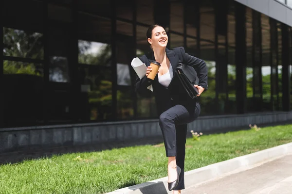 Щаслива бізнес-леді тримає портфель і каву, щоб піти під час бігу на вулиці — стокове фото