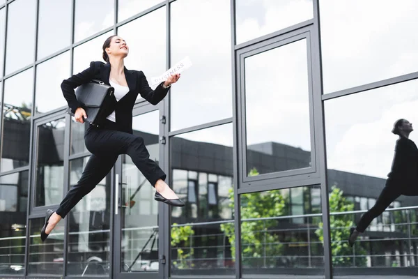 Beautiful businesswoman levitating while holding briefcase and newspaper — Stock Photo