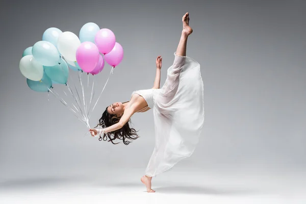 Graziosa ballerina in abito bianco che balla con palloncini festivi su sfondo grigio — Foto stock