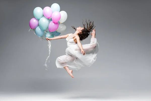 Beautiful ballerina in white dress dancing with festive balloons on grey background — Stock Photo