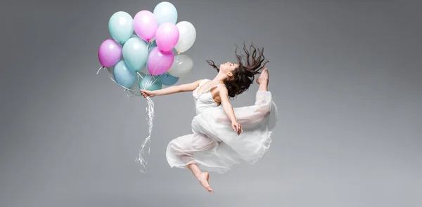 Panoramic shot of graceful ballerina dancing with festive balloons on grey background — Stock Photo