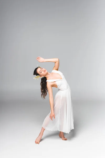 Bailarina elegante y atractiva en vestido blanco bailando sobre fondo gris - foto de stock