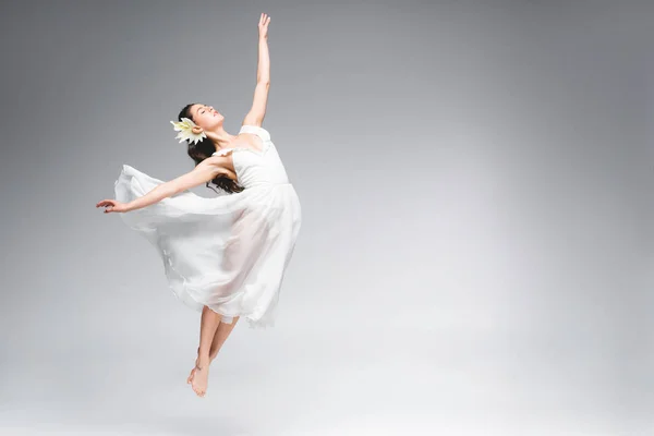 Graciosa bailarina em vestido branco pulando enquanto dança em fundo cinza — Fotografia de Stock