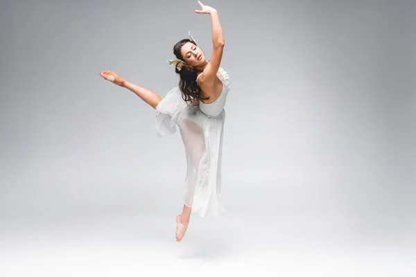 Молода красива балерина в білій сукні стрибає на сірому фоні — стокове фото