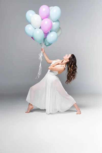 Anmutige, schöne Ballerina, die mit festlichen Luftballons auf grauem Hintergrund tanzt — Stockfoto