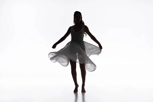 Молода витончена балерина в білій сукні танцює на сірому фоні — стокове фото