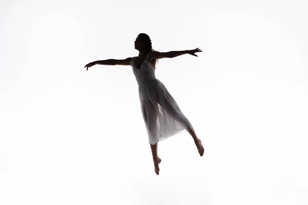 Молодая, изящная балерина прыгает, танцуя на белом фоне — стоковое фото