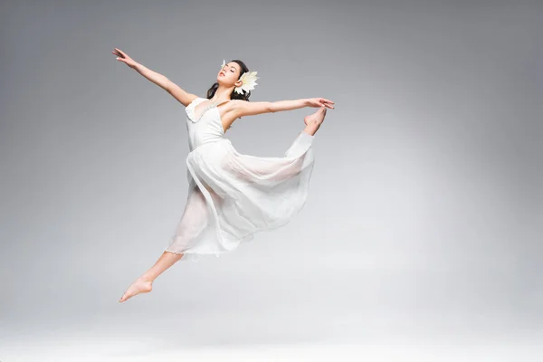 Hermosa bailarina joven en vestido blanco bailando sobre fondo gris - foto de stock