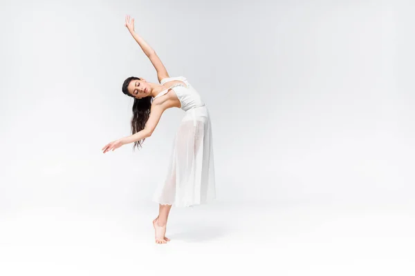 Beautiful ballerina in white dress dancing with closed eyes on grey background — Stock Photo