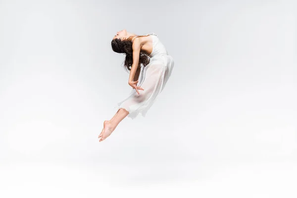 Side view of graceful young ballerina jumping in dance on grey background — Stock Photo