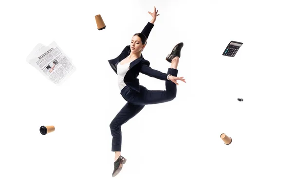 Молодая деловая женщина танцует в окружении летающей газеты, бумажные стаканчики, калькулятор и степлер изолированы на белом — стоковое фото