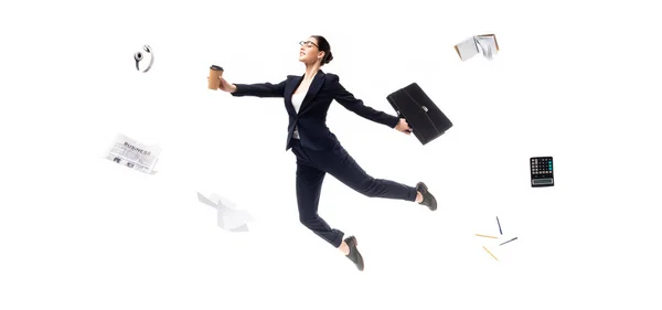 Panoramic shot of businesswoman holding coffee to go and briefcase while levitating surrounded headphones, newspaper, calculator and stationery isolated on white — Stock Photo