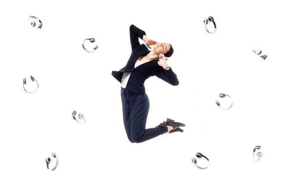 Young businesswoman levitating surrounded with flying headphones isolated on white — Stock Photo