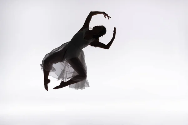 Молодая изящная балерина прыгает в танце на сером фоне — стоковое фото