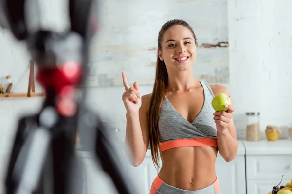 Enfoque selectivo de niña feliz sosteniendo manzana y señalando con el dedo - foto de stock