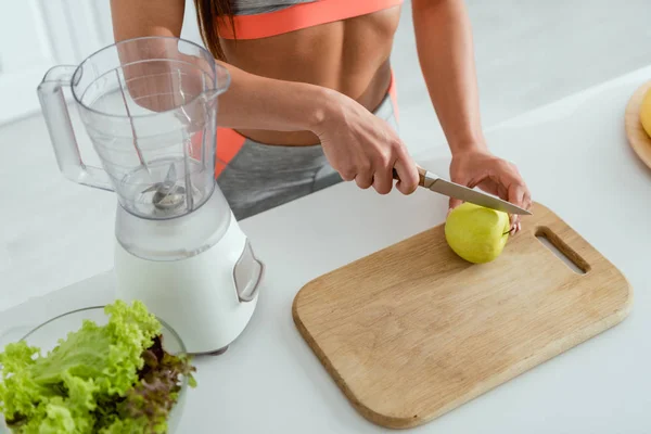 Overhead view of sportive girl cutting apple on chopping board — Stock Photo