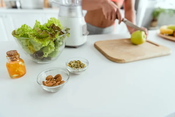 Selective focus of bowls with almonds and pumpkin seeds near bottle with oil and woman — Stock Photo