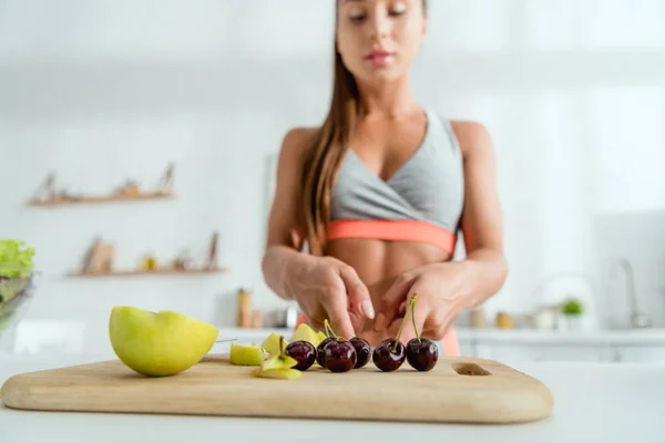 Selective focus of woman standing near apples and sweet cherries on cutting board — Stock Photo