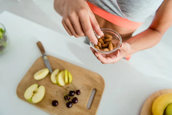 Vista aerea della ragazza che tiene ciotola con mandorle vicino tagliere con frutta — Foto stock