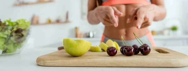 Panoramic shot of girl pointing with fingers at fruits on cutting board — Stock Photo