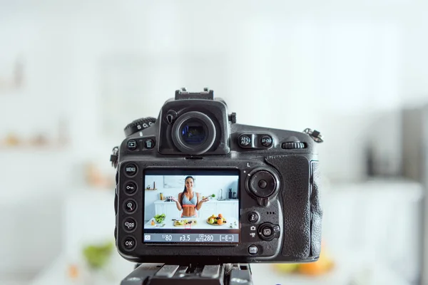 Selective focus of digital camera with happy girl gesturing near fruits on screen — Stock Photo