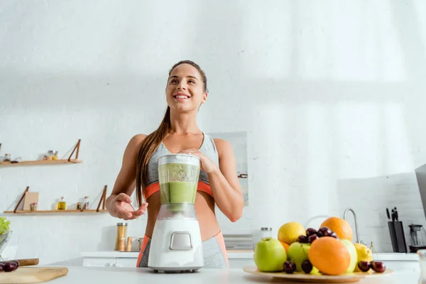 Vista de ángulo bajo de la mujer alegre cerca de la licuadora con batido - foto de stock