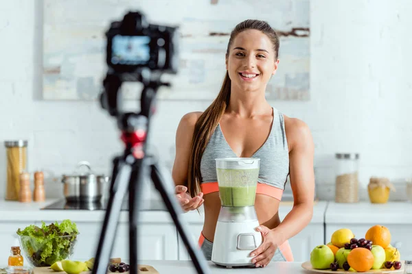 Selective focus of cheerful sportswoman gesturing near smoothie in blender — Stock Photo