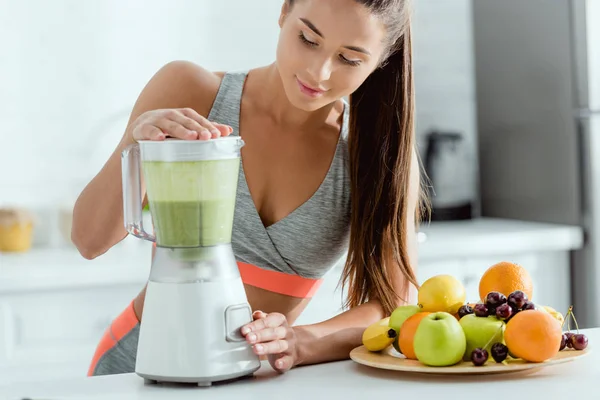 Selective focus of cheerful sportswoman preparing smoothie in blender — Stock Photo