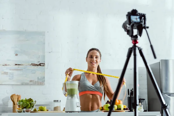 Enfoque selectivo de chica alegre sosteniendo cinta métrica cerca de frutas y cámara digital - foto de stock