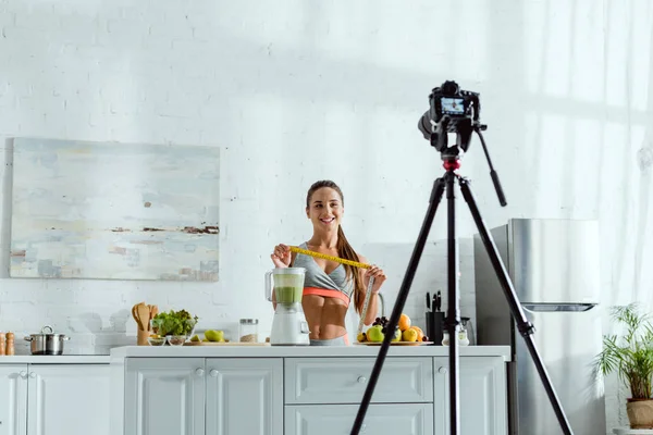 Messa a fuoco selettiva della donna allegra che tiene il nastro di misurazione vicino a frutta e fotocamera digitale — Foto stock