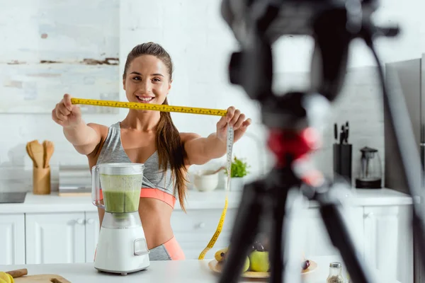 Selective focus of attractive sportswoman holding measuring tape near fruits and digital camera — Stock Photo